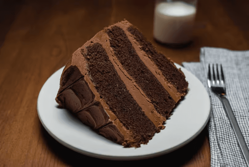 A thick slice of layered chocolate cake with rich chocolate frosting served on a white plate
