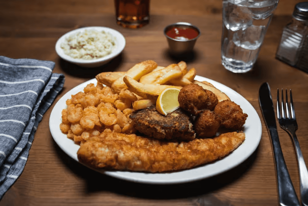 A plate of fried chicken, shrimp, and french fries served with dipping sauce and a side of rice